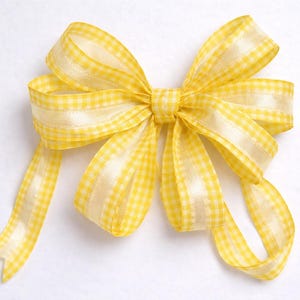 May include: A decorative yellow gingham ribbon bow with a satin finish. The bow features a classic design with multiple loops and tails, perfect for gift wrapping or crafting projects.