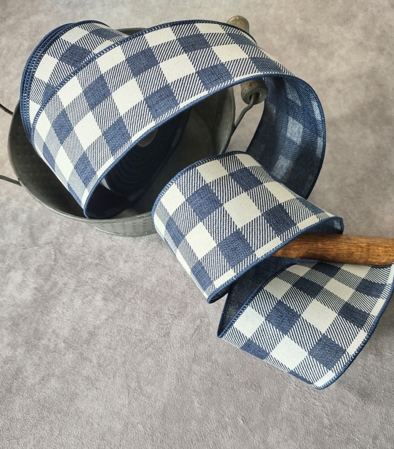 May include: A roll of blue and white checkered ribbon. The ribbon is a wide, decorative style with a gingham pattern. The ribbon is displayed in a metal bucket with a wooden handle. The ribbon is a perfect accent for crafts and gift wrapping.
