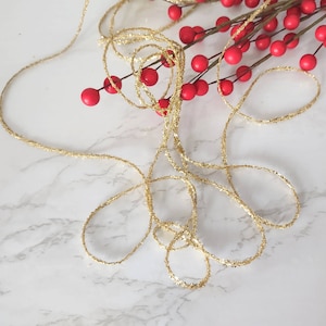 May include: Gold glitter ribbon with a red berry garland. The ribbon is coiled and the garland is draped over the ribbon.
