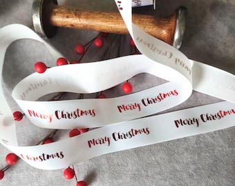 May include: White satin ribbon with the words "Merry Christmas" printed in red foil. The ribbon is wrapped around a wooden spool and decorated with red berries.