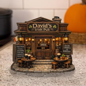 以下が含まれることがあります： 木造のファサード、ライトアップされた窓、石畳のベースを備えた「David's Irish Pub」の詳細なミニチュア。看板には「David's Irish Pub」と書かれています。テーブルとスツールが前にあります。パブにはアイルランドの旗とメニューボードがあります。