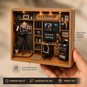 Peut inclure: Un diorama miniature en bois représentant un studio de photographie avec un appareil photo sur trépied, un bureau avec écrans, une chaise et des étagères. L'enseigne indique Alex Morgan Photographer Studio et 15 mm d'épaisseur de contreplaqué.