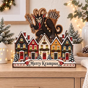 May include: A wooden tabletop decoration featuring a row of five colorful houses with lit windows and a large Krampus figure standing above them. The base is decorated with red flowers and the text Merry Krampus in a black serif font.