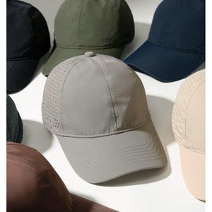 May include: A collection of baseball caps in various solid colors including gray, olive green, navy blue, black, brown, and beige. Each cap features a structured front panel, a curved brim with stitched detailing, and perforated side panels.