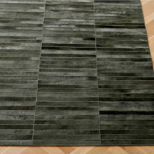 Könnte beinhalten: Ein rechteckiger, dunkelgrüner Teppich mit Patchwork-Design. Der Teppich besteht aus horizontalen Streifen, die eine strukturierte Oberfläche bilden. Er liegt auf einem hellbraunen Holzboden. Maße in Zentimetern.