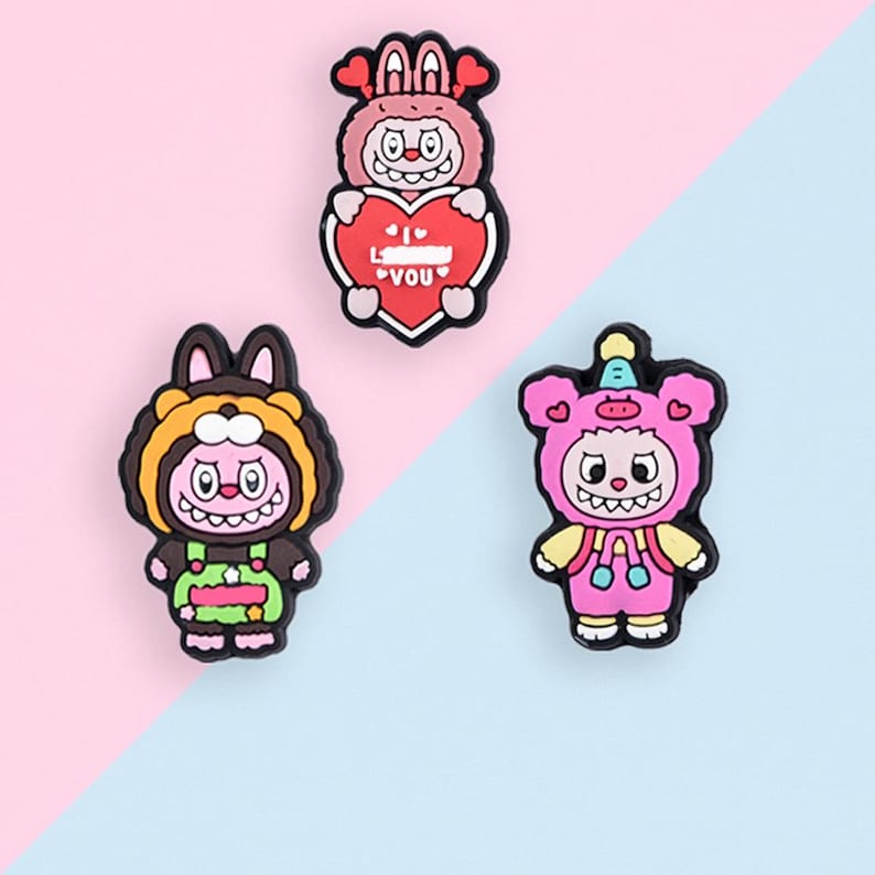 Puede incluir: Tres colgantes de personajes de dibujos animados coloridos. Un personaje rosa sostiene un coraz&oacute;n rojo con el texto "I YOU". Los otros dos personajes est&aacute;n vestidos con disfraces de animales, uno en marr&oacute;n y amarillo, el otro en rosa.