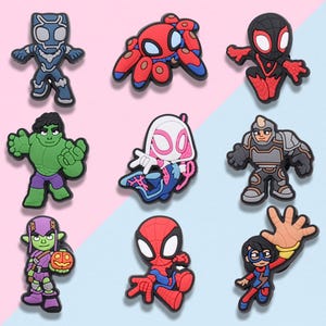 May include: A set of nine colorful rubber shoe charms featuring various comic book characters, including figures in red, blue, green, purple, and black, designed with distinct poses and expressions for attachment to footwear accessories.
