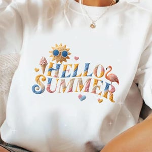 Puede incluir: Sudadera blanca con la frase bordada "HELLO SUMMER" en colores vibrantes. El diseño incluye un sol con gafas de sol, un helado, un flamenco y corazones. Una prenda casual con temática veraniega.