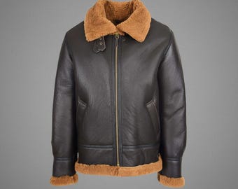 May include: A dark brown leather jacket with a tan shearling collar and trim. The jacket features a zip-up front, two front pockets, and a buckled collar strap. The jacket's design is classic and timeless, suitable for various occasions.