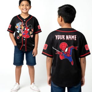 A young boy wearing a black baseball jersey with a Spiderman design and the text "YOUR NAME" printed on the back.