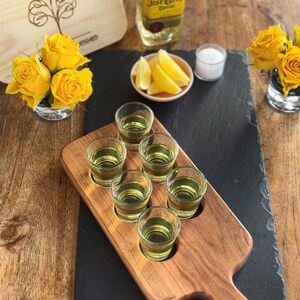 May include: A wooden serving tray with six shot glasses filled with a yellow liquid. A bottle of tequila, lemon wedges, salt, and yellow roses are also present. The word "Cherry" is written on the image.