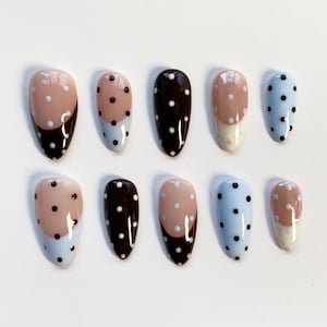 May include: A collection of ten oval false nails. The designs include solid dark brown, light blue with white polka dots, and a two-tone design with a light brown top and dark brown bottom. Each nail is approximately 2 cm long.