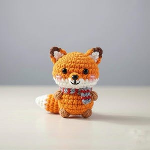 May include: A crocheted fox figurine with orange, white, and brown yarn. The fox has a white and red scarf, black eyes, and pink cheeks. The fox's tail is white-tipped. The fox is a handmade item.