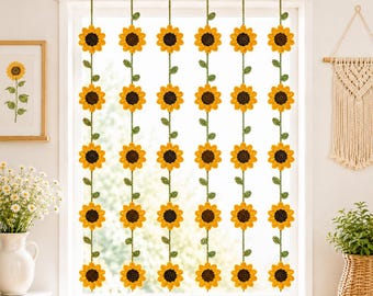 May include: A window hanging featuring six vertical strands of crocheted sunflowers. Each strand consists of yellow and brown sunflower blossoms connected by green stems with small leaves, all suspended from a horizontal wooden rod.