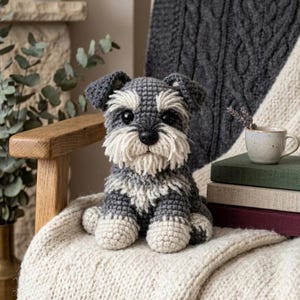 Pode incluir: Um cão Schnauzer de crochê feito à mão em tons de cinza e branco, com barba e patas fofas. O bicho de pelúcia está sentado em um cobertor creme, com uma estética aconchegante e artesanal. Um item decorativo charmoso.