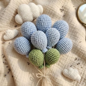 Può includere: Un gruppo di palloncini all'uncinetto fatti a mano in tonalità blu e verde, legati con spago. Diverse nuvole all'uncinetto bianche sono sparse intorno ai palloncini, creando un'estetica morbida e stravagante. Ideale per una cameretta.