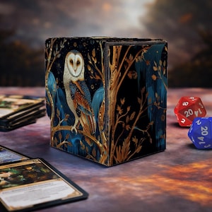 May include: A square card storage box with an owl illustration. The box has a dark blue background with gold and teal accents. Two multi-sided dice are visible in the background, along with a few trading cards.