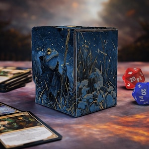 Puede incluir: Caja de dados ilustrada en azul y dorado con un mago rana sosteniendo un bastón, sobre un fondo de noche estrellada. Se ven cartas y dados.