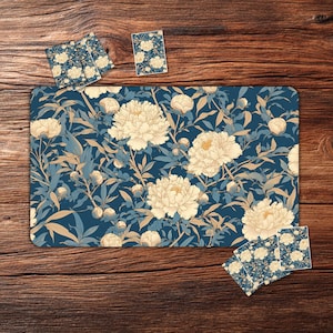 Può includere: Un tappetino da gioco con motivo floreale blu con sottobicchieri abbinati. Il tappetino presenta grandi fiori di peonia color crema e foglie su uno sfondo blu scuro. I sottobicchieri hanno lo stesso design. Il set è esposto su una superficie di legno.