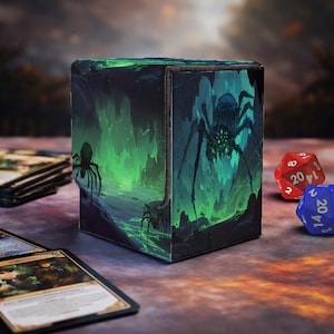 Puede incluir: Una caja de almacenamiento de cartas en forma de cubo con un diseño de araña de fantasía en tonos verdes y negros. La caja está decorada con una ilustración detallada de una araña en un entorno de cueva. Dos dados y algunas cartas están junto a la caja.