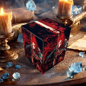 May include: A cube-shaped box with a red and black illustration of a figure holding a sword. The box has a white stripe on top. The image is set on a wooden table with candles, books, and crystals.