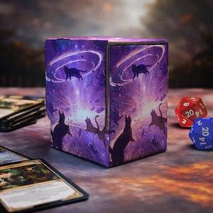 May include: A rectangular deck box featuring a vibrant purple cosmic space design with multiple silhouettes of black cats floating amidst swirling nebulae, glowing rings, and scattered debris, with a textured fabric-like finish on the exterior.