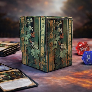 Op de afbeelding: Een rechthoekige kaartenbox met een verticaal streeppatroon in tinten groen, goud en zwart, bedekt met een botanische print van groene bladeren en kleine rode bessen. De box heeft een scharnierend deksel en een gestructureerde afwerking.