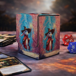 Puede incluir: Una caja para cartas rectangular con una ilustración impresa de un conejo blanco con sombrero de mago marrón y capa roja, sosteniendo un bastón. La caja tiene una superficie texturizada y muestra al personaje en el frente y el lateral.