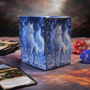 Op de afbeelding: Een rechthoekige deckbox met een blauw-witte illustratie van een witte wolf omringd door gloeiende blauwe energie en sneeuwvlokken. De doos heeft een magnetische klepsluiting en toont hetzelfde wolfontwerp op de voor- en zijpanelen.