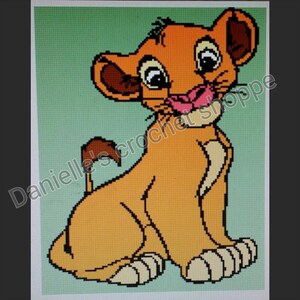 May include: A pixelated cross-stitch pattern of a young lion cub with orange fur, a cream-colored chest, and dark brown ear details. The cub has large eyes and a pink nose, set against a light green background with the text Danielle's crochet shoppe.