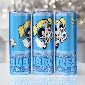 Puede incluir: Tres vasos aislados azules con el personaje de dibujos animados Burbuja de Las Supernenas. Cada vaso tiene una base azul brillante con el nombre "Bubbles" en letras de burbujas. El personaje está representado con coletas rubias y un vestido blanco.