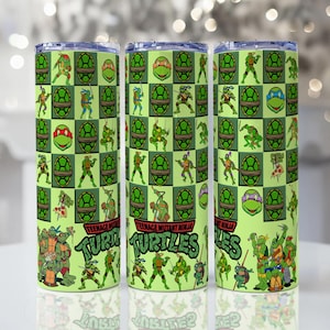 Könnte beinhalten: Drei grüne und gelbe isolierte Becher mit Teenage Mutant Ninja Turtles. Das Design umfasst die Schildkröten, ihre Masken und die Worte "Teenage Mutant Ninja Turtles". Die Becher haben ein Schachbrettmuster mit den Schildkröten und ihren Masken.