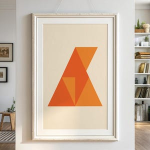 Puede incluir: Gran impresión artística abstracta enmarcada con un diseño geométrico en tonos naranja sobre un fondo crema. La obra de arte está en un marco blanco, colgada en una pared blanca. La habitación tiene suelo de madera y está bien iluminada.