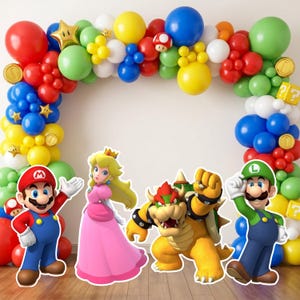May include: A balloon arch featuring red, blue, green, yellow, and white balloons with gold star, coin, and question block accents. Mario, Princess Peach, Bowser, and Luigi character cutouts are positioned in front of the balloon display.