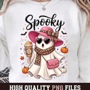 May include: A white sweatshirt featuring a graphic of a ghost wearing a pink hat with a leopard print bow, heart-shaped sunglasses, and a leopard print scarf. The ghost holds a coffee cup labeled Fall Fuel and carries a pink quilted purse.