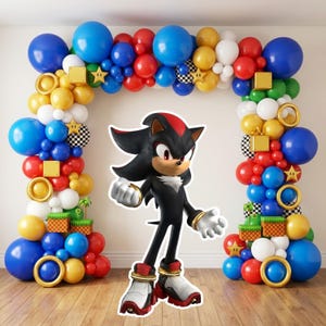 May include: A large balloon arch featuring blue, red, yellow, white, and green balloons, accented with gold rings, yellow stars, and checkered spheres. A large, flat, die-cut cardboard cutout of the character Shadow the Hedgehog stands in the center.