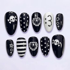 May include: A set of ten press-on nails featuring a black and white color palette. Designs include white skulls and crossbones, polka dots, heart-shaped lace frames, a colon and number three emoticon, stars, and horizontal stripes on a glossy finish.