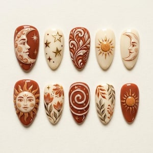 May include: A set of ten almond-shaped press-on nails featuring a celestial and botanical theme. The designs include raised 3D motifs of suns, crescent moons with faces, stars, swirling patterns, and floral elements in shades of terracotta, cream, and brown.