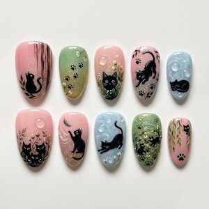 May include: A set of ten press-on nails featuring various artistic designs of black cats. The nails display pink, green, and light blue backgrounds with painted details including cat silhouettes, paw prints, foliage, and clear water droplets.