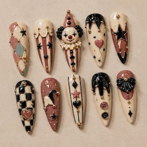 May include: A set of ten almond-shaped press-on nails featuring a circus-inspired theme. Designs include a 3D clown face, black and white checkered patterns, harlequin diamonds, stars, hearts, buttons, and gold metallic accents on cream and mauve bases.