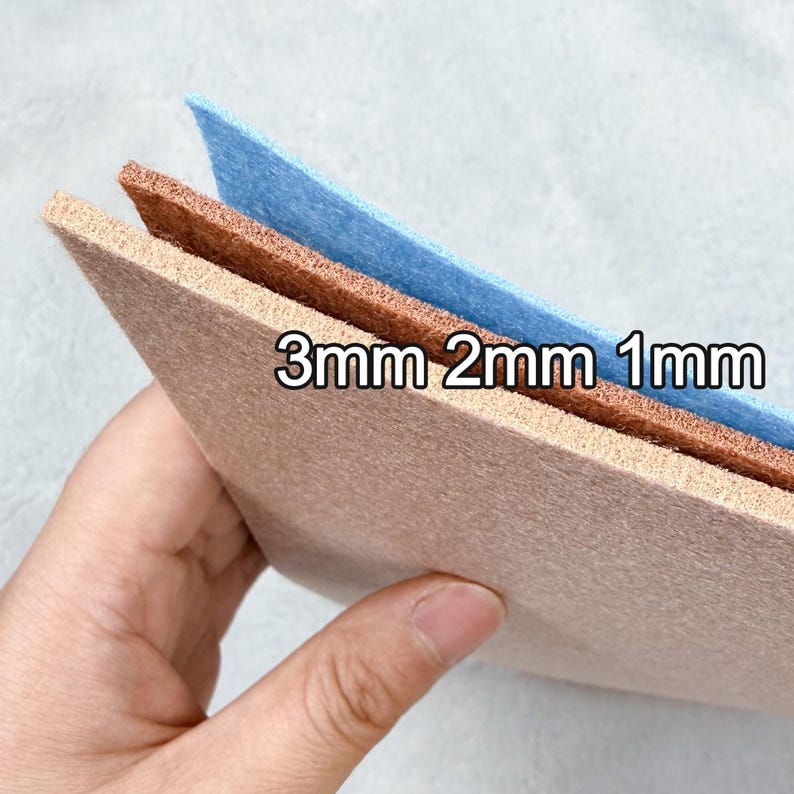 May include: Three sheets of felt in beige, brown, and blue, with thicknesses of 1mm, 2mm, and 3mm, are stacked. The text "3mm 2mm 1mm" is printed on the felt. The felt is held by a hand.