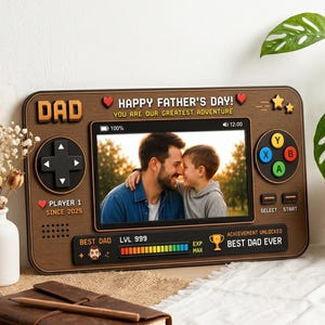 May include: A wooden Father's Day picture frame in the shape of a retro video game controller. The frame features a photo of a father and child, with text that reads "Happy Father's Day!" and "Best Dad Ever."