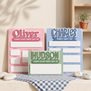 May include: Three rectangular school milestone signs in pink, blue, and green. The pink sign says Oliver, the blue sign says Charles, and the green sign says Hudson. Each sign features raised lettering and blank white spaces for writing details.