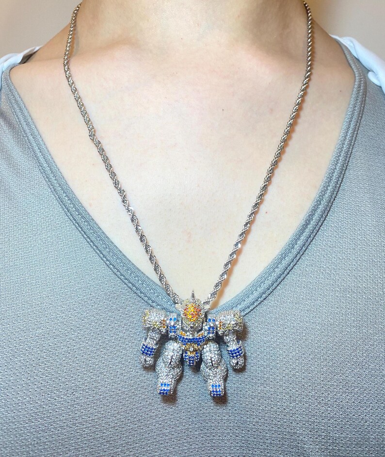 May include: Silver-toned necklace with a robot pendant. The pendant is encrusted with clear, blue, and yellow gemstones. The chain has a twisted rope design. The robot pendant has detailed arms, legs, and a head.