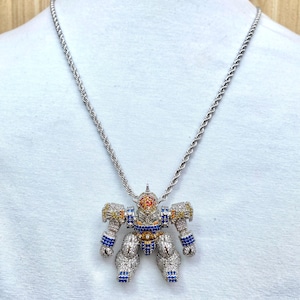 May include: Silver-toned robot pendant necklace. The robot pendant is encrusted with clear, blue, yellow, and orange gemstones. The necklace chain is a silver rope style.