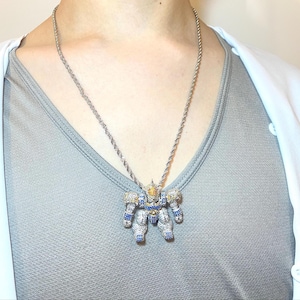 May include: Silver-toned robot pendant necklace. The robot pendant is encrusted with blue, yellow, and clear gemstones. The necklace chain is a twisted rope design. The robot has a detailed design with articulated arms and legs.