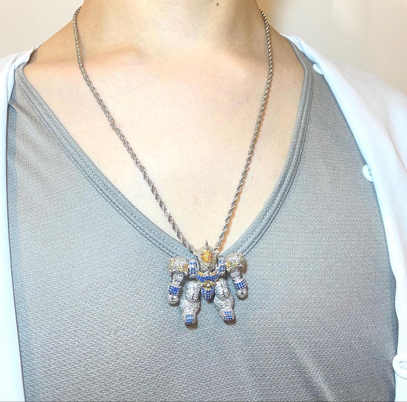 May include: Silver-toned robot pendant necklace. The robot pendant is encrusted with blue, yellow, and clear gemstones. The necklace chain is a twisted rope design. The robot has a detailed design with articulated arms and legs.