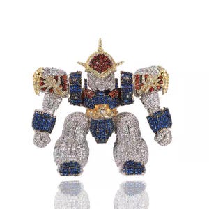 May include: A robot-shaped brooch, encrusted with sparkling gemstones. The brooch features a silver body, blue and red accents, and gold detailing. The robot's head is adorned with red and gold stones.