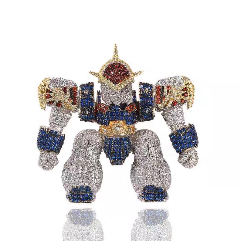 May include: A robot-shaped brooch, encrusted with sparkling gemstones. The brooch features a silver body, blue and red accents, and gold detailing. The robot's head is adorned with red and gold stones.