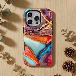 以下が含まれることがあります： 大理石模様のカラフルな携帯電話ケース。ケースは、青、オレンジ、赤、紫、金色の色が混ざっています。携帯電話ケースは光沢のある仕上がりで、カメラの切り抜きがあります。